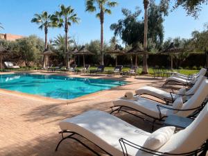 una piscina con sedie a sdraio bianche e palme di Villa Singulière By Louhou Collection a Marrakech