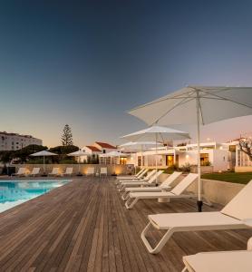 a row of lounge chairs and umbrellas next to a swimming pool at Ericeira Prime Villas in Ericeira