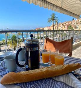 a table with a tea kettle and glasses of orange juice at Le Garavan-vue mer-plage-clim-terrasse in Menton