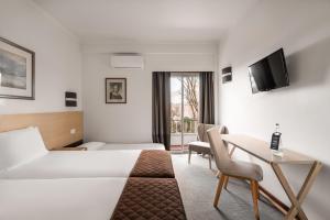una camera d'albergo con letto, scrivania e TV di Crisol Tres Pastorinhos a Fátima