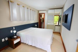 1 dormitorio con 1 cama blanca y TV en Flamingo Beach - Rede Soberano, en Porto Seguro