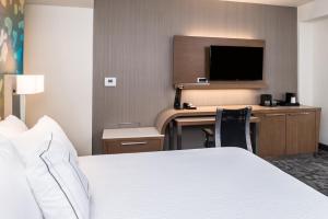 a hotel room with a bed and a desk with a television at Courtyard by Marriott Detroit Farmington in Farmington Hills