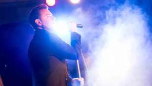 een man zingt in een microfoon op een podium bij Oakdene Forest Park Violet 1 in Saint Leonards