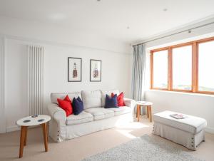 Una sala de estar blanca con un sofá blanco y almohadas rojas y azules. en Bryn Deryn, en Criccieth