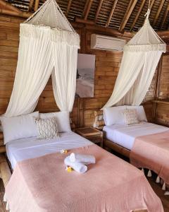 2 Betten in einem Zimmer mit weißen Vorhängen in der Unterkunft Bamboo Bungalows in Nusa Lembongan