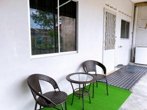 3 sillas y una mesa en un porche con alfombra verde en Mirahani Homestay Melaka, en Melaka