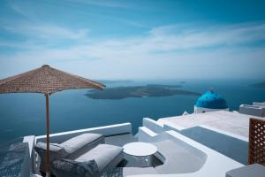 a patio with chairs and an umbrella and the water at Cilon Suites Santorini in Imerovigli