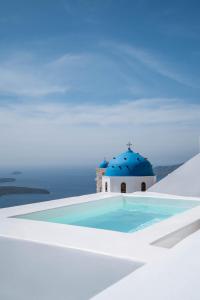 a swimming pool with a blue roof and a church at Cilon Suites Santorini in Imerovigli