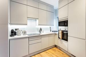uma cozinha branca com armários brancos e piso em madeira em Gorgeous Roehampton Flat em Londres