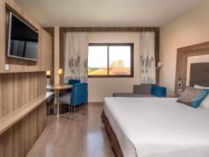 a hotel room with a bed and a table and a window at Novotel Campo Grande in Campo Grande