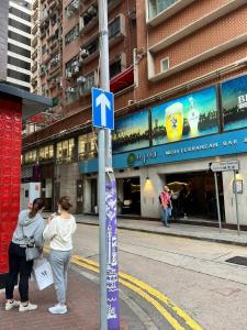 dwoje ludzi stojących obok znaku ulicznego na ulicy miejskiej w obiekcie SAAN INN w Hongkongu