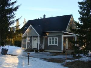 a small house with a black roof in the snow at Villa Kumpuharju in Nilsiä