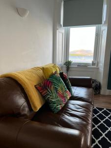 a brown leather couch with pillows on it in a living room at Beautiful Upper Apartment/Stunning Sea Views, Isle of Bute in Port Bannatyne