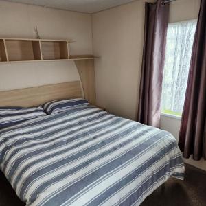 a bedroom with a striped bed and a window at 3 BEDROOM CARAVAN AT THE GRANGE HOLIDAY PARK, CHAPEL ROAD INGOLDMELLS in Addlethorpe
