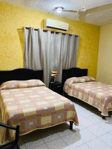 two beds in a room with yellow walls at Hotel Del Valle in El Naranjo
