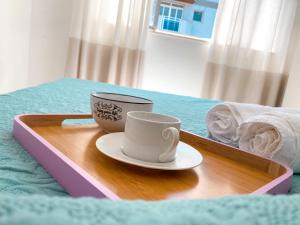 a tray with two coffee cups on a bed at Delicinha, a 5 minutos à pé da Praia do Forte in Cabo Frio