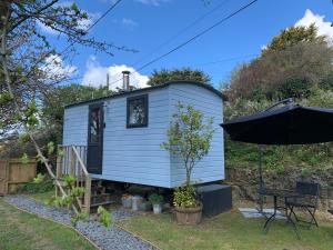 a blue tiny house with a table and an umbrella at Tides Reach, Deluxe Shepherds hut, 100m from the Beach in St Merryn