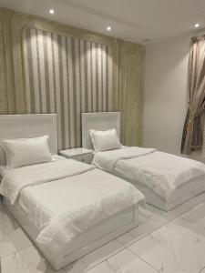 two beds in a bedroom with white sheets at منتجع قرية الريف الفندقية in Taif