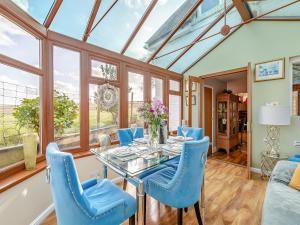 uma sala de jantar com uma mesa de vidro e cadeiras azuis em Brittons Hill Cottage em Wavehorne