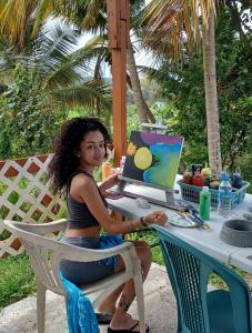 une femme assise à une table avec un ordinateur portable dans l'établissement Jubilee Campsite Swim & Paint, à Las Piedras