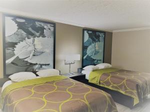two beds in a hotel room with paintings on the walls at Super 8 by Wyndham Picayune in Picayune