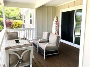 a porch with two chairs and a table and a surfboard at Mākaha House in Waianae