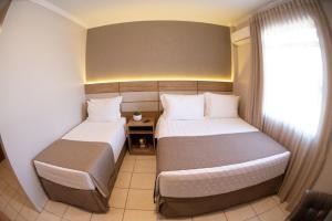 a hotel room with two beds and a window at Hotel Capital Das Pedras in Teófilo Otoni