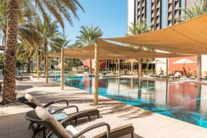 een zwembad met tafels en stoelen en een gebouw bij Sheraton Oman Hotel in Muscat