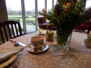 a table with a cup and a vase of flowers on it at Rose Cottage in Tunstall