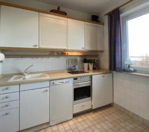 cocina con armarios blancos, fregadero y ventana en Haus Seelöwe Wohnung 1, en Wittdün