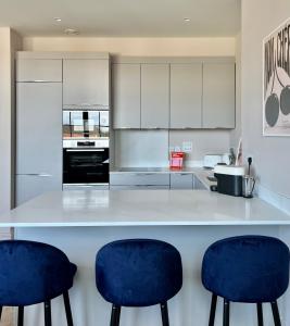 a kitchen with white cabinets and blue bar stools at The Apartments Lytham Square in Lytham St Annes