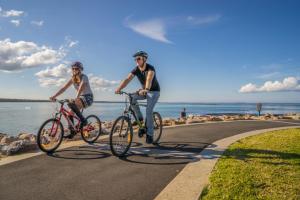 two men riding bikes on a road near the water at Paradise Bungalow Waterfront in Sanctuary Point