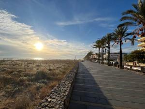 a boardwalk leading to the beach with palm trees at Precioso Bajo en 2a línea de mar in Segur de Calafell