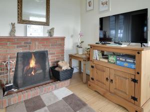 a living room with a fireplace and a television at Curlew Cottage in Thorpe Saint Peter