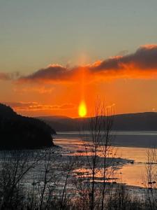 a sunset over a body of water with the sun setting at Suite 2, Flèche du fjord, vue Saguenay, Mont Valin in Saint-Fulgence