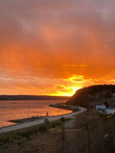 un coucher de soleil sur une étendue d'eau avec une route dans l'établissement Suite 2, Flèche du fjord, vue Saguenay, Mont Valin, à Saint-Fulgence