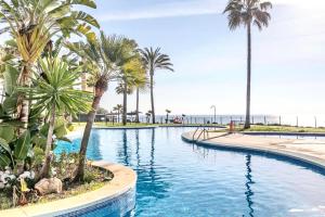 a swimming pool with palm trees and the ocean at MI CAPRICHO BEACHFRONT- 9D Apartment with sea views - Costa del Sol in La Cala de Mijas