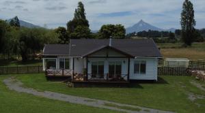 a small white house with mountains in the background at Hospedaje Familiar El Encanto in Puyehue