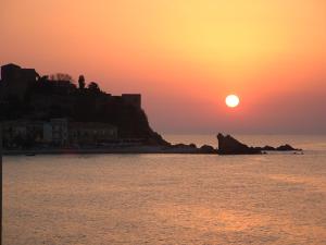 a sunset over the ocean with a person standing on a cliff at Perla di Mare in Castel di Tusa