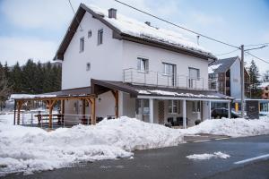 a white house with snow on the side of a street at Guest House Mylan in Ličko Petrovo Selo