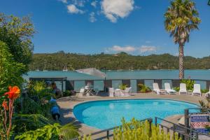 a pool in a yard with chairs and a palm tree at Oceans 88 Whitianga Coastal Suites in Whitianga