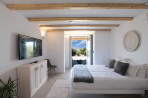 a white bedroom with a bed and a tv at Mykonos Village in Ano Mera