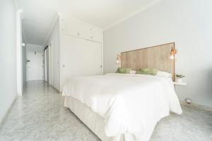 a white bedroom with a large white bed with a wooden headboard at El 5º Cielo in Las Palmas de Gran Canaria