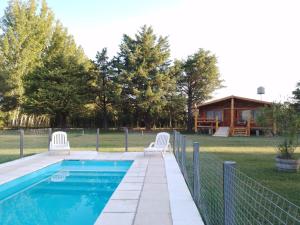 une piscine avec deux chaises blanches et une maison dans l'établissement Cabañas Las Acacias, à Colonia Las Rosas