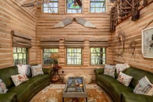 a living room with wooden walls and green couches at "Magical Treehouse" w spiral slide off the deck 350 acres on the Brazos River! Tubing! Petting Zoo! in Weatherford