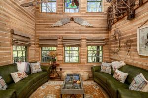 una sala de estar con paredes de madera y sofás verdes. en "Magical Treehouse" w spiral slide off the deck 350 acres on the Brazos River! Tubing! Petting Zoo! en Weatherford