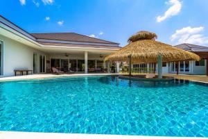 una piscina con ombrellone di paglia accanto a una casa di Luxury 7 Bedroom Pool Villa! (WL67) a Hua Hin