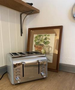 a toaster oven sitting next to a picture of a plant at The Painter’s Retreat in Lower Boscaswell