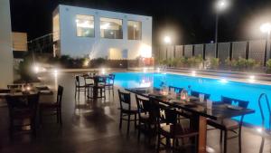 a restaurant with tables and chairs next to a swimming pool at night at Manjeera Sarovar Premiere in Rājahmundry