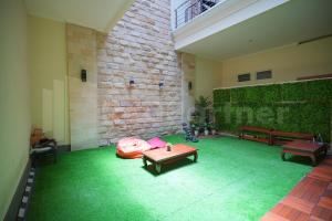Habitación con suelo de moqueta verde, bancos y pared de ladrillo. en One & Quin Guest House Syariah Mitra RedDoorz, en Jenggrik